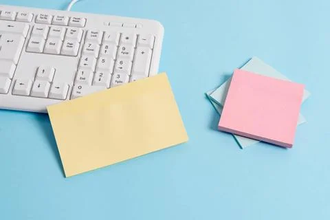 Light blue desk with different sizes of empty paper notes, computer keyboa... Stock Photos