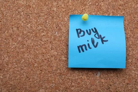 Light blue paper note with phrase Buy Milk on cork board, closeup. Space fo.. Stock Photos