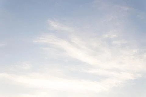 Light blue sky with feather-like clouds lit by the rays of the early sun Stock Photos