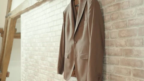 Light brown groom's suit jacket hanging on a stone wall in a beautiful room Stock Footage 317098325