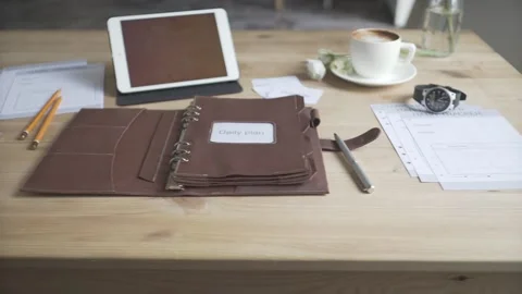 Light brown wooden table work space area desktop with leather case note pad jour Stock Footage 137538683