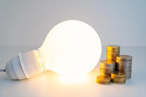 Light bulb and coins next to it. Energy costs. Stock Photos
