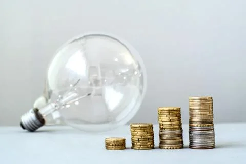 A light bulb and growing stacks of coins. Rising electricity costs, expenses. Fotos de archivo