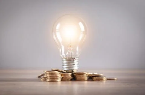 Light bulb and stack of coins on the desk. Saving energy and money Stock Photos