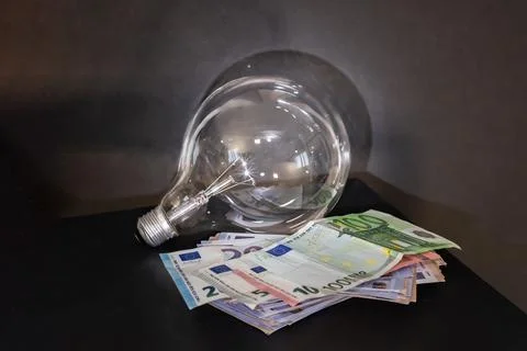 Light bulb and stack of euro banknotes. Electricity consumption, energy costs Foto stock
