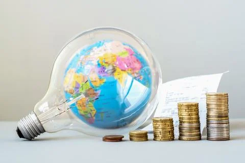 Light bulb with a globe inside and a growing stack of coins. Global energy Fotos de archivo