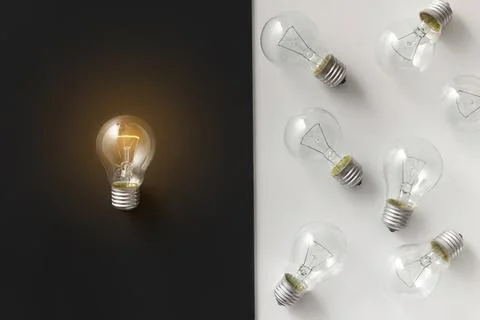 Light bulb glowing on dark background with others off Stock Photos