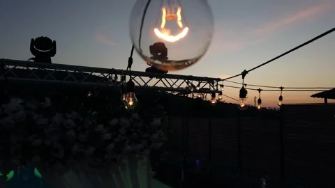 A light bulb is hanging from a wire. The light bulb is lit up and is glowing  Stock Footage 344915594