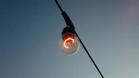 A light bulb is hanging from a wire. The light bulb is lit up and is glowing  Stock Footage 344915606