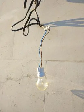 The light bulb hangs against a light concrete wall, illuminated by sunlight Stock Photos