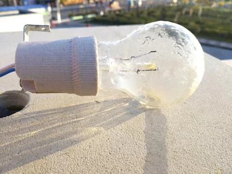 The light bulb hangs against a light concrete wall, illuminated by sunlight Stock Photos