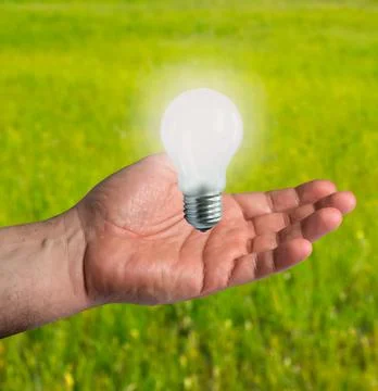 Light bulb in a man's hand on the background of a green field Stockfoto's
