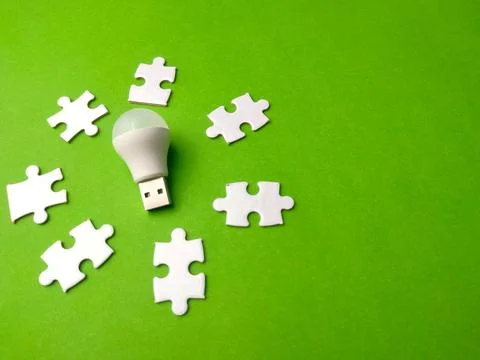 Light bulb placed on a green surface surrounded by white puzzle pieces Stock Photos