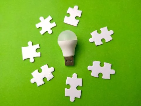 Light bulb placed on a green surface surrounded by white puzzle pieces 写真素材
