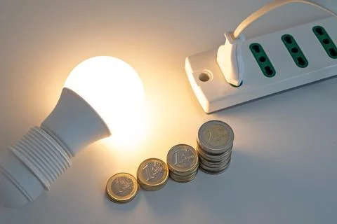 Light bulb on, with plug and coins next to it. Energy costs. Stock Photos