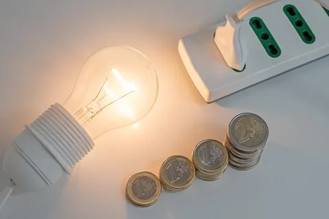 Light bulb on, with plug and coins next to it. Energy costs. Stock Photos