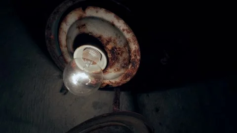 The light bulb is screwed into a rusty ceiling close-up glows in a dark room Stock Footage 201611254