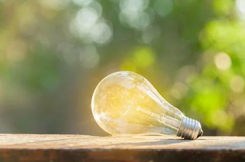 A light bulb shining brightly placed on a wooden floor Bokeh background scene Stock Photos