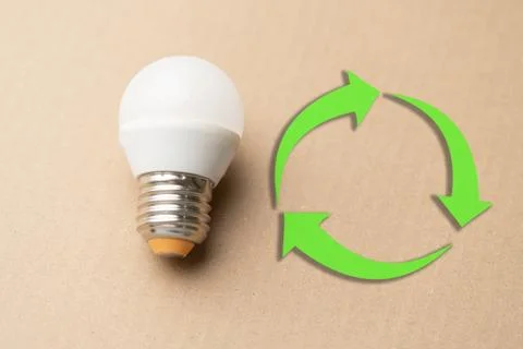 A light bulb is on a table next to a green recycling symbol Stock Photos