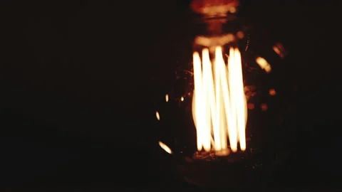 Light bulb Warm yellow light over dark black background. Bright glowing Edison Stock Footage 194571179