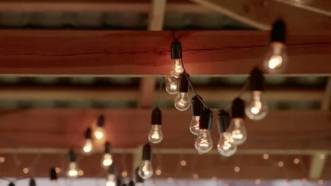 Light bulbs garland close up. Electric bulb shine hanging on wall as decoration Vidéo 76565313