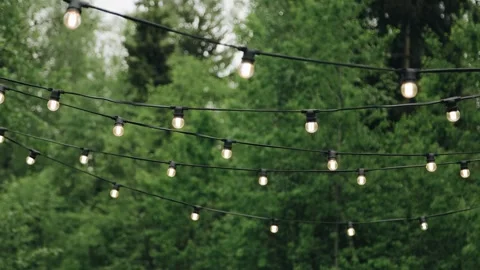 Light bulbs hang on wires in the yard and illuminate the surrounding space Stock Footage 260717858
