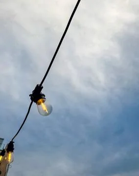 Light bulbs on strings against blue sky with clouds. Stock Photos