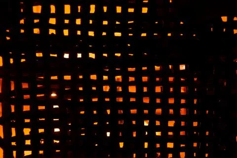 The light of a candle is visible through a fine straw mesh in the dark, backg Stock Photos