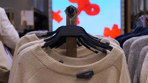 A light colored sweater with an open top and an anti-crane rivet on a hanger in Stock Footage 314033845