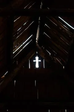 Light cross shape hole in dark room on old wood wall near roof. Stock Photos