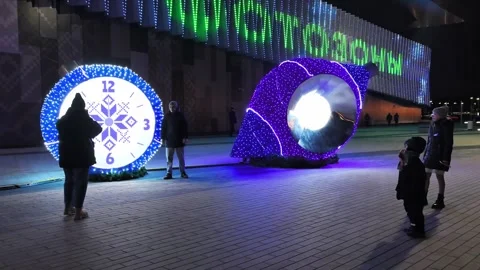 Light display shows clock and shell at night in a city square Stock Footage 325806436