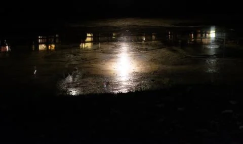 The light emanating from a street lamp is reflected in the muddy water Stock Photos