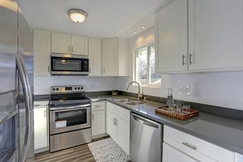 Light filled home interior features small compact kitchen with white cabinets Stock Photos