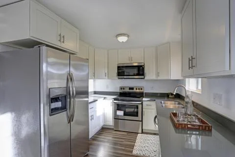 Light filled home interior features small compact kitchen with white cabinets Stock Photos