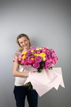 On light gray background a young blonde girl with a large bouquet of pink peony Stock Photos