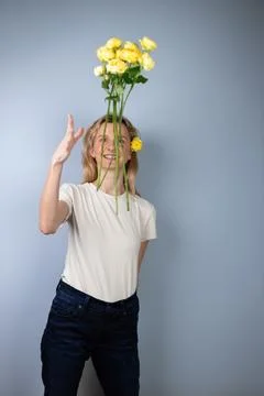 On light gray background a young blonde girl in a light T-shirt throws peony Stock Photos
