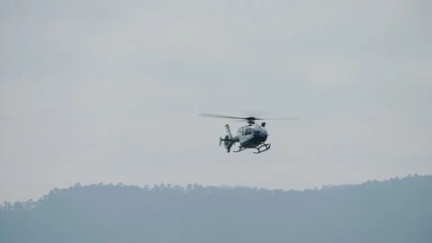 Light gray helicopter in flight over hazy forested hillside 動画素材 336450659