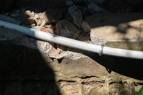 Light gray or white plastic PVC pipe situated in a shallow trench Stock Photos