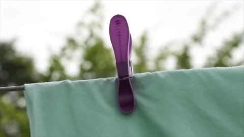 Light green blue bed sheet hanging on clothesline with purple plastic clip Stock Footage 248713814