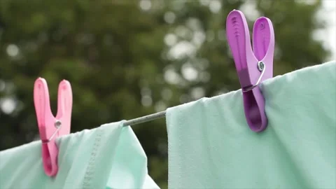 Light green blue bed sheets hanging on clothesline with pink and purple clips Video stock 248713897