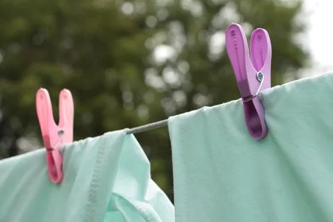 Light green blue bed sheets hanging on clothesline with pink and purple clips Stock Photos