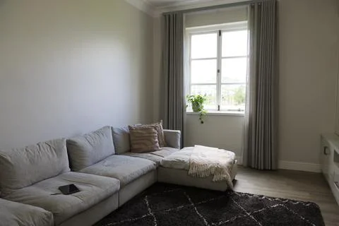 Light grey L shape sectional sofa is anchoring living room with pillows, fringed Stock Photos
