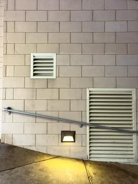 Light illuminates a section of a wall with two vents and a railing next to a  Stock Photos