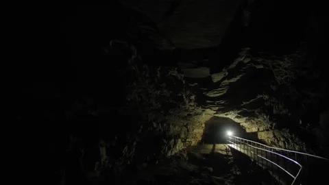 A Light moving through a Cave lighting up a Dark Passageway Stock Footage