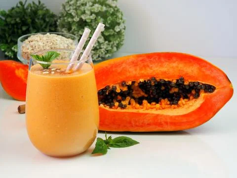 Light orange smoothie on the background of half a papaya. Stock Photos