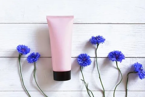 Light pink squeeze bottle plastic tube with black cap, blue cornflowers flowers Stock Photos