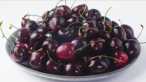 On a light plate of ripe dark red cherries rotating in a circle on a white .. 库存影片 298604268