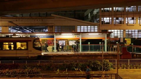 Light rail train arriving at outdoor station platform at night in Tuen Mun Видео 341110145