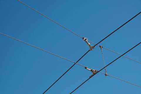 Light rail train cables cross in clear blue sky. Stock Photos