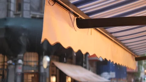 Light rain drizzles on cafe awning while patrons seek shelter nearby Stock Footage 306315531